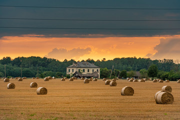 A field with straw bales after harvest during sunset.