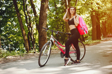 Naklejka premium Cute girl standing in a autumn forest. Lady use the map. Woman with pink backpack. Famale with bicycle.