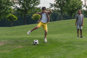 Obraz premium cute african american boy standing on grass near friend playing football