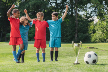 Obraz na płótnie Canvas selective focus of multicultural kids gesturing near trophy and football