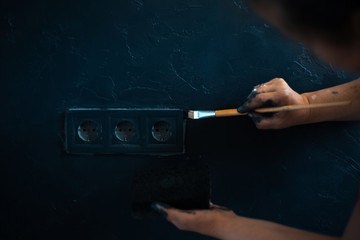 Close-up of female hands with brush paint power socket with black color.