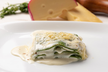 Homemade fresh baked spinach sheets lasagna with bechamel and cheese sauce in a white plate. Soft light