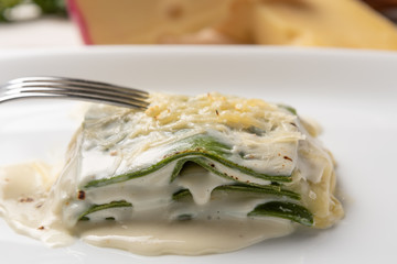 Homemade fresh baked spinach sheets lasagna with bechamel and cheese sauce in a white plate. Soft light