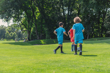 Naklejka premium back view of curly boy playing football with friends on grass