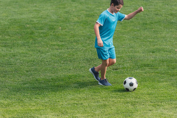 cute boy in sportswear playing football on green grass