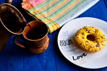 Homemade Turkish coffee, a Turk for cooking, a ceramic cup, a kitchen napkin, donuts on a white plate on a blue background in the kitchen.