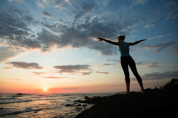 Young fitness woman practicing yoga on the ocean coast during a amazing sunset.