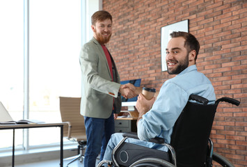 Obraz premium Young man in wheelchair with colleague at office