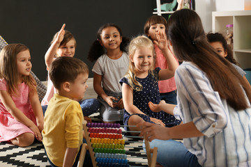Cute little children with nursery teacher in kindergarten. Indoor activity
