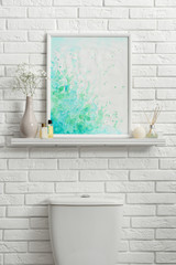 Shelf with picture on white brick wall above toilet bowl in restroom interior