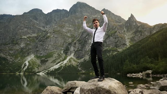 Successful confident businessman happy from the victory, crazy happy emotions near a lake in the rocky mountains at sunset, winning and successful deal concept