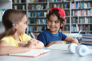 Little children writing at table with books in library reading room