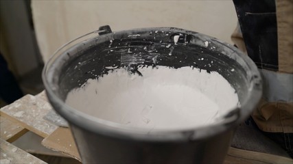 Worker puts plaster on a spatula from a bucket. Spatula with putty in hand. Worker takes putty from a bucket. Hand with a spatula in a bucket.