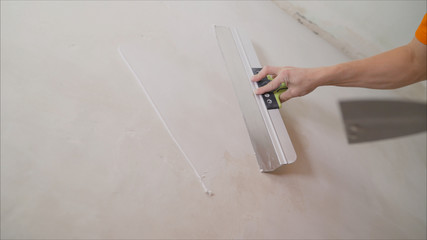 Worker spackles the walls with a spatula. Spatula with putty in hand. Worker puts of plaster on...