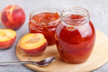Peach jam in a glass jar with fresh fruits on gray concrete background. side view.
