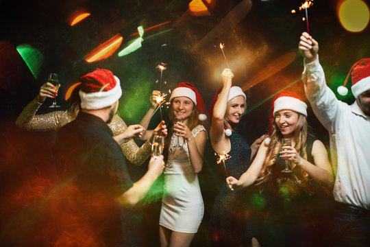 New Year party in night club, Christmas celebration atmosphere. Friends dancing with champagne glasses and sparkles, modern youth life