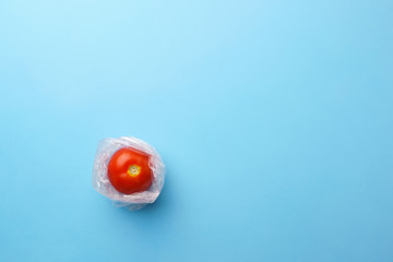 Tomato in plastic bag in blue background. Recycling and environment concept: fresh food in plastic package