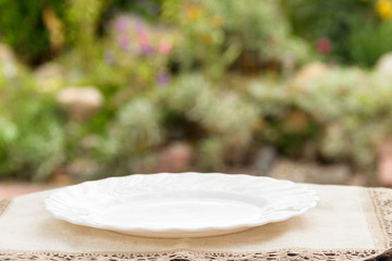 Empty plate on the table  with blurred green  garden on background. For montage product display or design key visual layout.