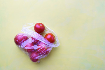 Tomatoes in plastic bag in blue background. Recycling and environment concept: fresh food in plastic package