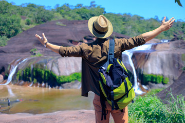 Happy man standing arms stretched. Atop the mountains and waterfalls in front, male tourists enjoy nature.