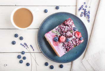 Berry cake with milk cream and blueberry jam on blue ceramic plate with cup of coffee and fresh blueberries on a white wooden background. top view.