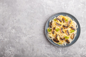 Rice noodles with champignons mushrooms, egg sauce and oregano on a gray concrete background. Top view.