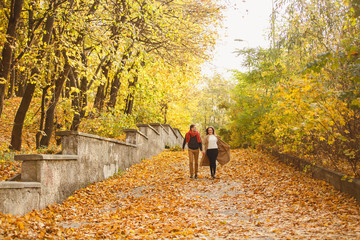 Fototapeta premium Couple weared in autumn-style clothes (oranfe scarf and vest) running through the autumn park. Alley covered with yellow foliage. Autumn walk outdoors. Two lovers in autumn park. Romantic dating