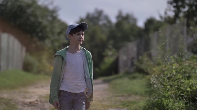 boy with a slingshot in pocket walks along a country road