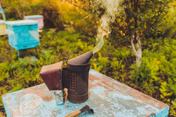 Beekeepers metal smoker smoking on the top of a beehive. The silver smoker has green bellows with...