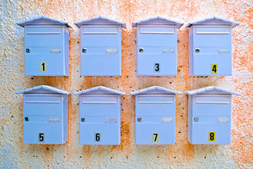 Eight letter boxes on a wall, waiting for a snail mail love letter.