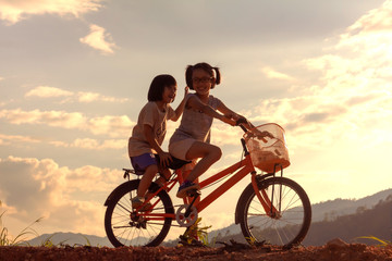 Obraz premium Silhouette two children playing riding bike on mountain at sunset sky background