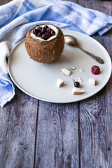 Berry dessert with yogurt in a cup of coconut on a wooden background. Blackberries, raspberries, blueberries, black currants. Blue napkin