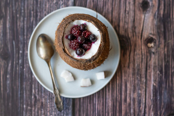 Berry dessert with yogurt in a cup of coconut on a wooden background. Blackberries, raspberries, blueberries, black currants.