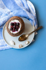 Berry dessert with yogurt in a cup of coconut on a blue background. Blackberries, raspberries, blueberries, black currants. Blue napkin