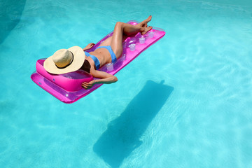 Woman in blue bikini and straw hat floating in turquoise pool
