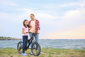 Woman and her little daughter with bicycle near river