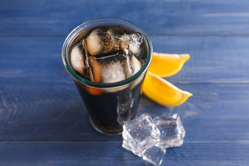Glass of fresh cola with ice and lemon on color wooden background
