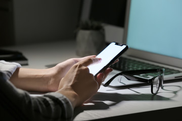 Woman with mobile phone working at table in evening