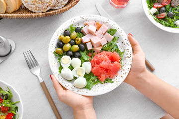 Woman holding plate with fresh salad at table, top view