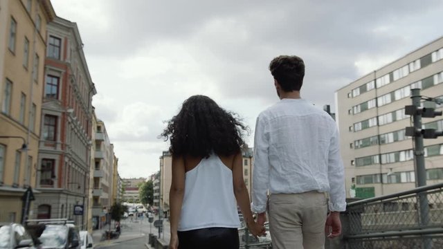 Medium shot of a young man and woman walking hand in hand on a street.