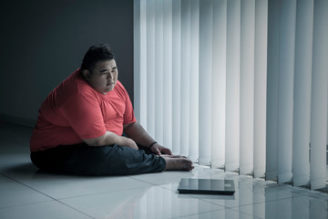 Overweight man looking at the scale near the window