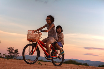 two children playing riding bike on mountain at sunset sky background