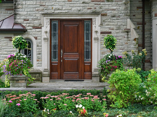 stone faced house with flower garden and elegant wooden front door with sidelights