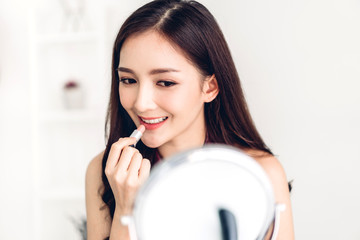 Smiling beautiful woman fresh healthy skin looking on mirror and enjoying applying lips with red lipstick at home.facial beauty and cosmetic concept
