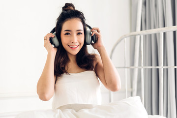 Beautiful young asia woman relaxing listening to music with  headphones on bed at home