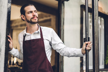 Portrait of handsome bearded barista man small business owner smiling outside the cafe or coffee shop.Male barista standing at cafe
