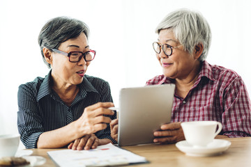 Portrait of two friend happy senior adult elderly asia women smiling and working with digital tablet computer at home.Retirement concept