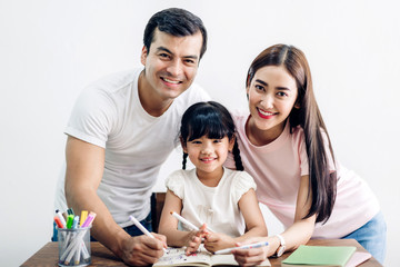 Happy family father and mother with daughter  learning and writing in notebook with pencil making homework at home.Education concept