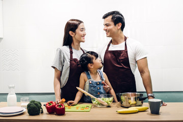 Happy family father and mother with daughter cooking and preparing meal together in the kitchen