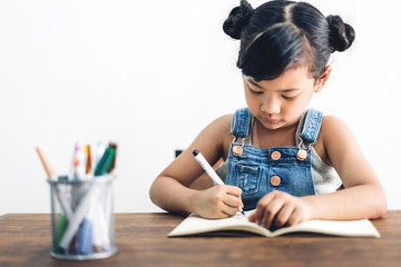 School kid little girl learning and writing in notebook with pencil making homework at home.Education concept
